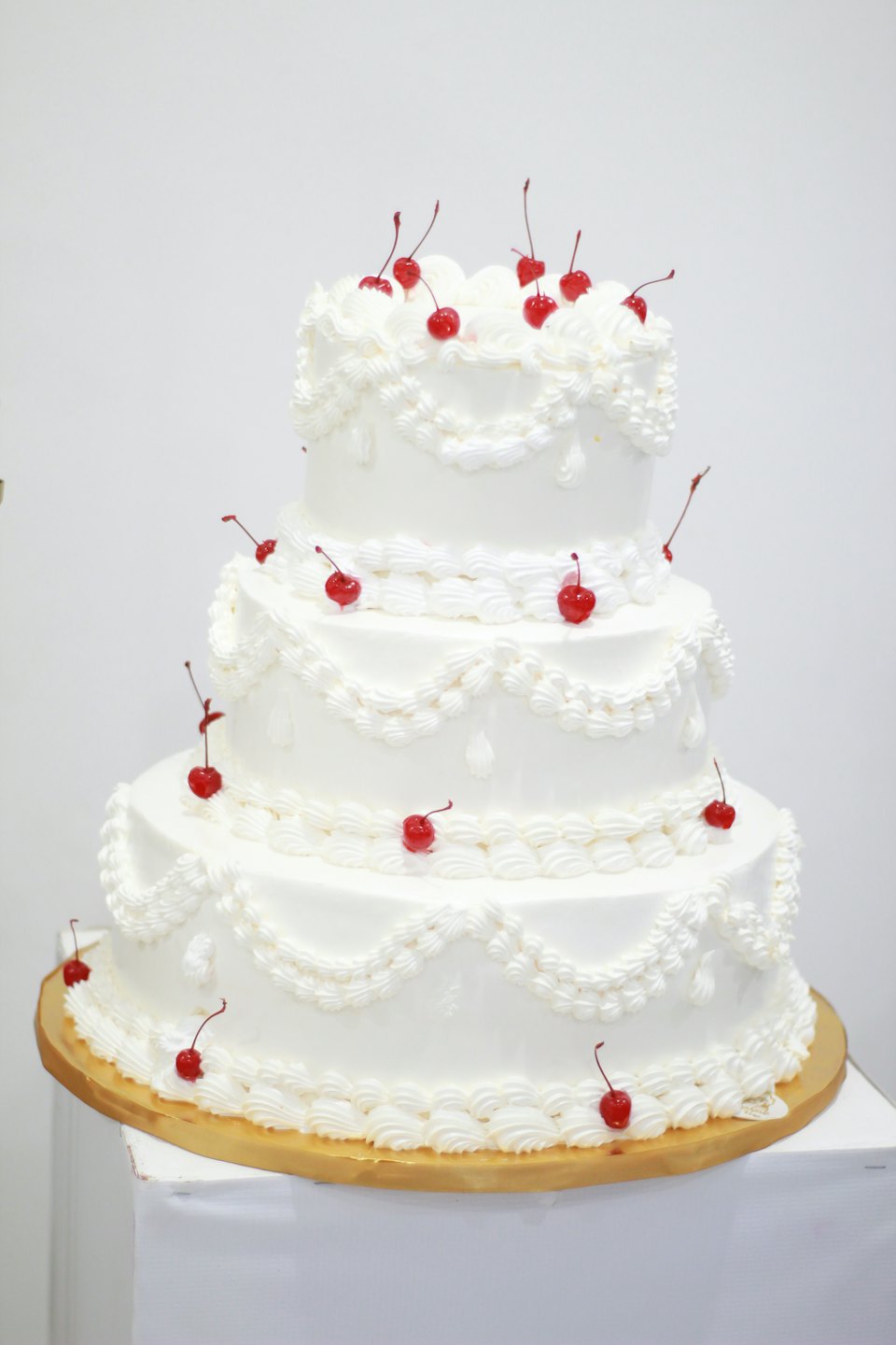 Four-tiered white cake decorated with red cherries on a golden board.