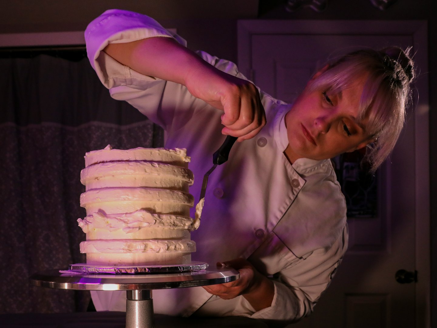 Baker applying white frosting to a tiered cake.